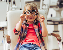 Маленький хлопчик сидить у кріслі дитячого лікаря-офтальмолога в універсальній пробній оправі для перевірки зору